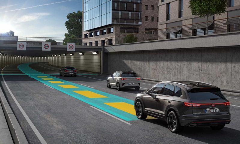 Ein dunkelgrauer VW Touareg fährt auf einer grün-gelben Linie eine Straße entlang auf einen Tunnel zu.