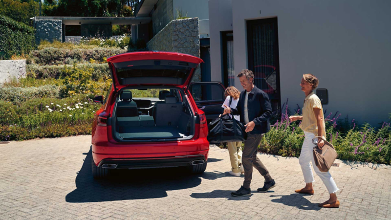 A man and a woman walk towards a VW Touareg with open luggage compartment.