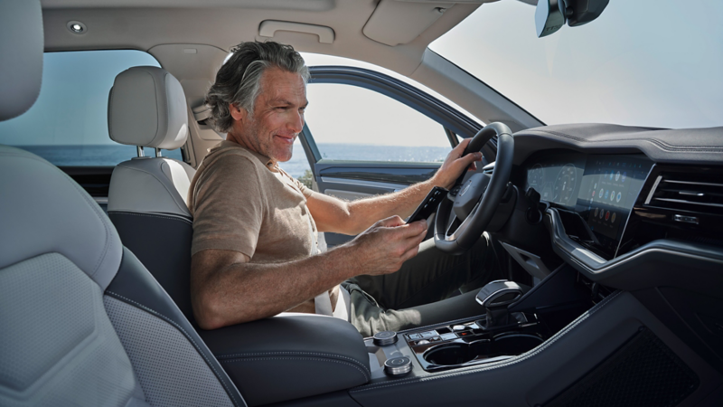 Ein Mann sitzt in einem Volkswagen mit einem Smartphone in der Hand.