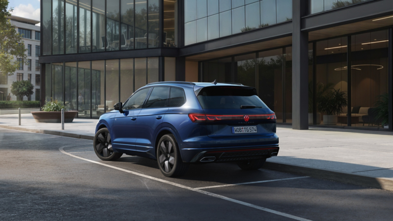 En blå VW Touareg FINAL EDITION visad snett bakifrån framför en kontorsbyggnad med glasfasad.