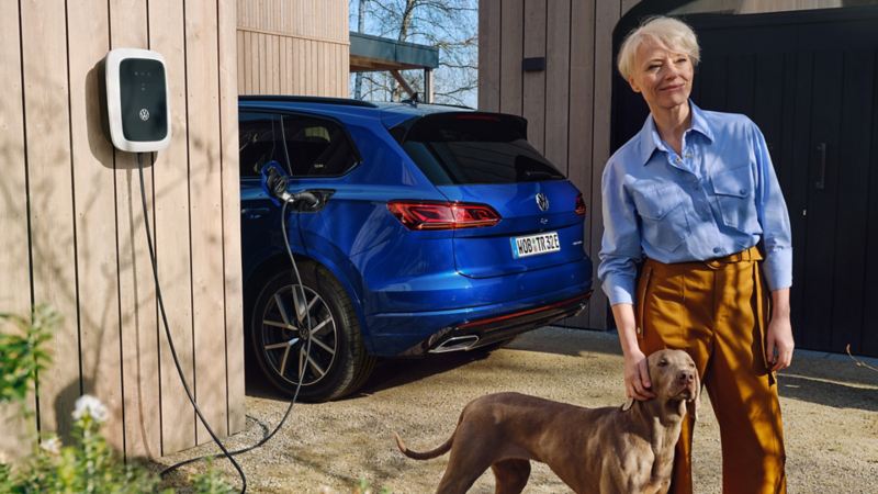 A woman stands with her dog in front of a loading VW Touareg eHybrid.