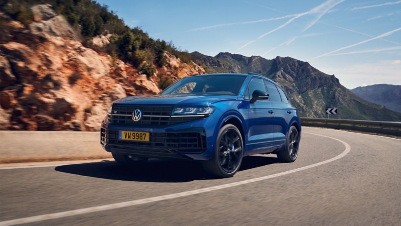 Le Touareg R bleu roule sur une route dans un paysage montagneux.