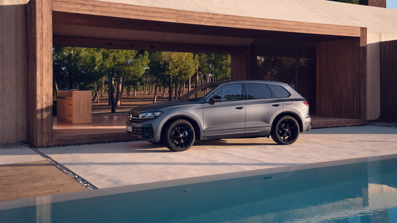 En grå VW Touareg R eHybrid står parkerad utanför en carport