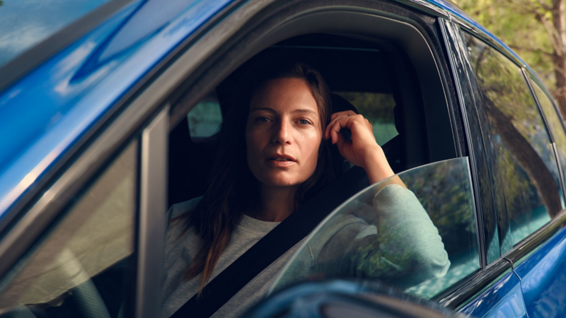 Madame est assise sur le siège conducteur d'un Touareg R et a entrouvert la fenêtre par laquelle elle regarde par-dessus.