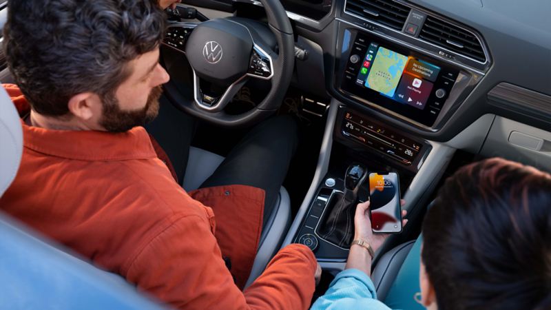 A woman turning on Wireless Apple CarPlay® while a man holding a steering wheel