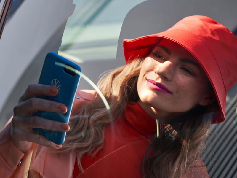 A person dressed in red using a smartphone in front of a red vehicle, reflected in the rear side window.