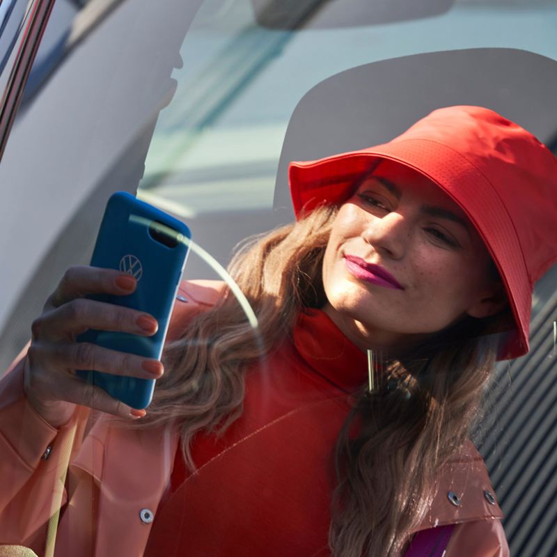 A person dressed in red using a smartphone in front of a red vehicle, reflected in the rear side window.