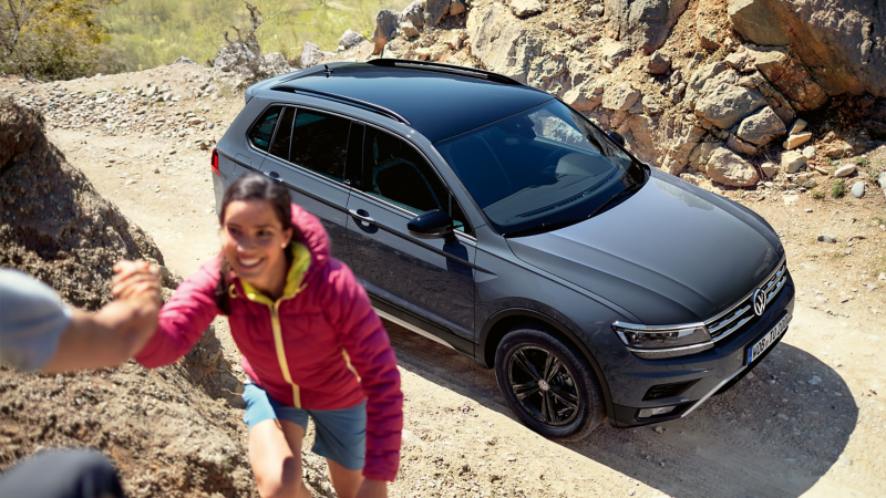 Une VW Tiguan Offroad vue d’en haut, de biais, une femme grimpe sur un rocher.