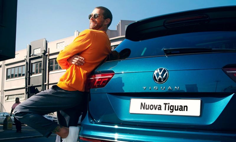 Un uomo con gli occhiali da sole si appoggia a Volkswagen Nuova Tiguan.