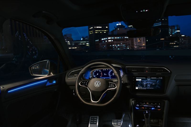 Cockpittet i kabinen i VW Tiguan om natten, på farvedisplayet ses indstillingerne til ambientebelysningen (ekstraudstyr), kabinen stråler i et blåt lys.