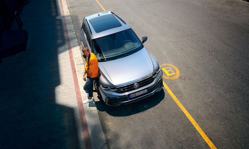 Un homme s'appuie contre l'avant d'un Nouveau Tiguan R-Line "Black Style"