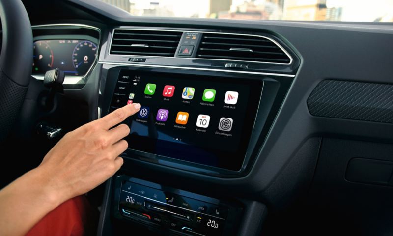 Infotainment-System im VW Tiguan mit App-Connect Ansicht, eine Hand nähert sich dem Touchscreen.