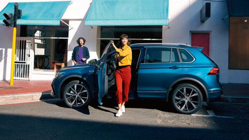 VW Tiguan parkt am Straßenrand, eine Frau steigt aus.