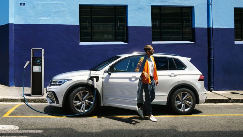 Volkswagen Tiguan hybride rechargeable en blanc, vue latérale, en charge au bord de la route, une personne descend
