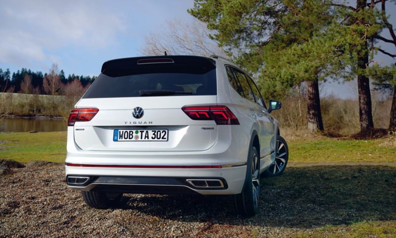 Ein weißer Volkswagen Tiguan R-Line Allspace steht auf einer Wiese, Blick auf das Heck. 