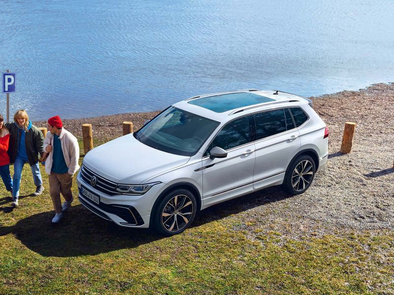 Άποψη του Tiguan Allspace σε λευκό χρώμα, με πανοραμική οροφή, σταθμευμένο στην όχθη μιας λίμνης. Μία παρέα 3 νέων περνούν μπροστά του.