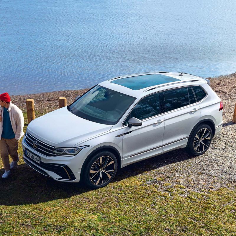 Άποψη του Tiguan Allspace σε λευκό χρώμα, με πανοραμική οροφή, σταθμευμένο στην όχθη μιας λίμνης. Μία παρέα 3 νέων περνούν μπροστά του.