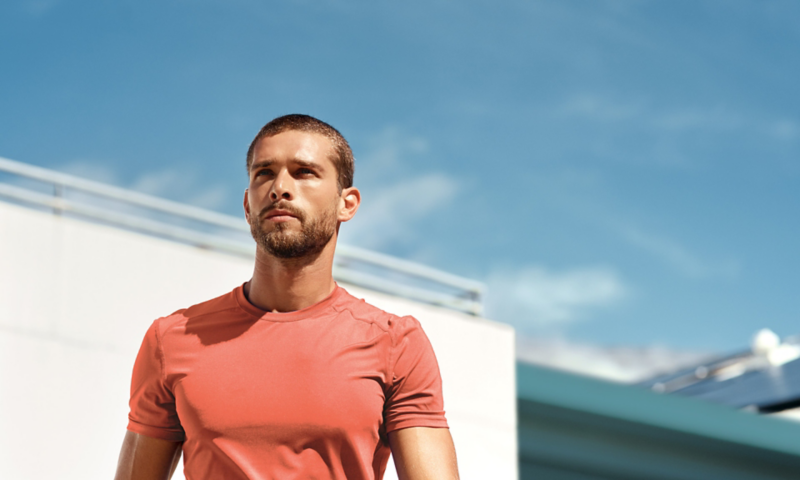 View on a young man in red sports t-shirt in front of a white building and blue sky. 