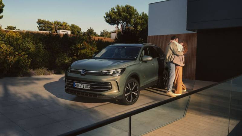 Zielony Tiguan widoczny z profilu, obok niego stoi para.
