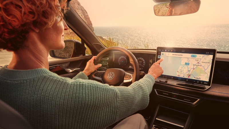 Detailed view of the large display in the VW Tiguan. One hand navigates on the screen from the driver seat.