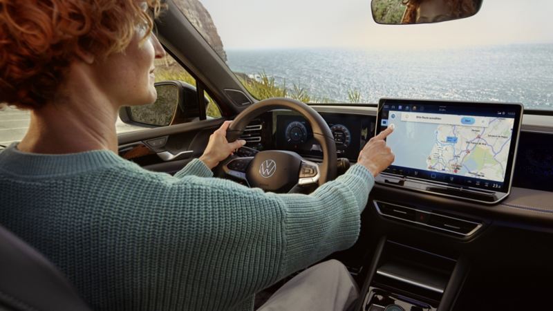Detaljbild av den stora skärmen i VW Tiguan. En hand navigerar på skärmen från förarsätet.