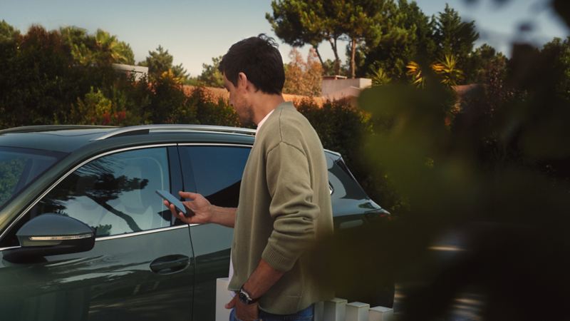 En person står foran en Volkswagen med en mobiltelefon i hånden