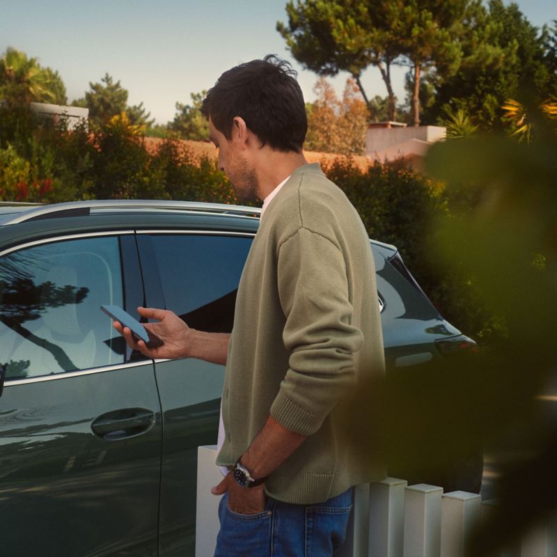 Person in front of a Volkswagen with a mobile phone in their hand