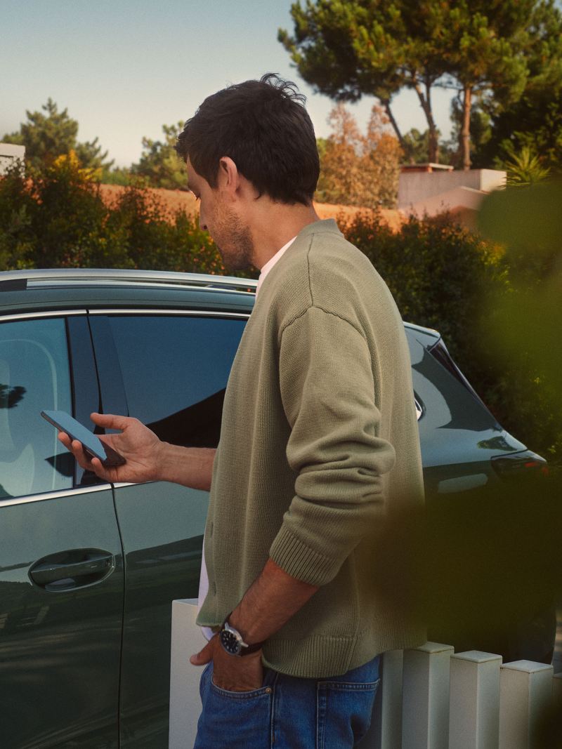 En person står framför en Volkswagen med en mobil i handen