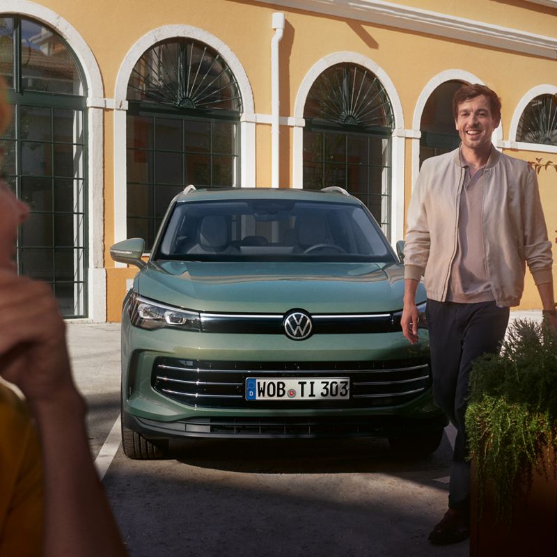 Une femme au premier plan regarde un homme marcher vers elle, devant le VW Tiguan de face.