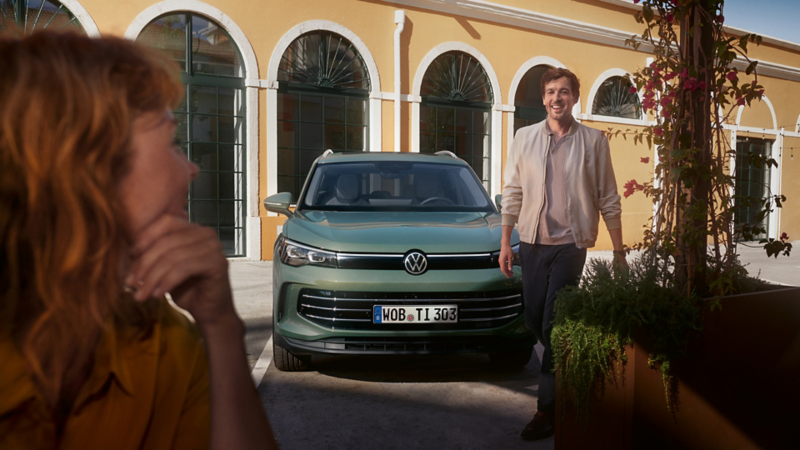 A young man smilingly walks away from a green Tiguan towards a young woman, who joyfully awaits him.