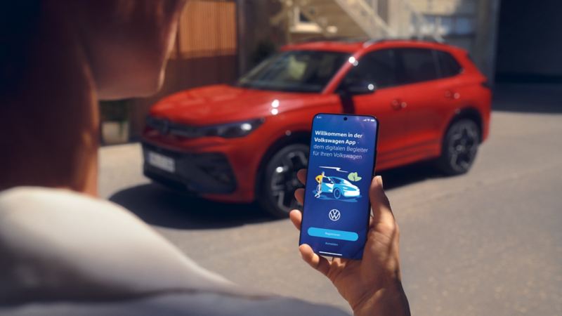 Blik op een smartphonescherm met voertuiggegevens van de Tiguan, op de achtergrond een zijwaarts geparkeerde rode VW Tiguan.
