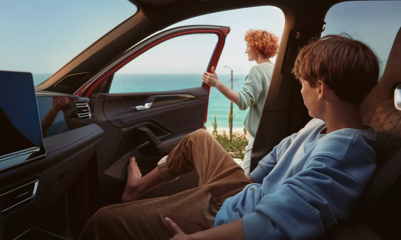 Ein junger Mann auf der Fahrerseite des dunkelgrünen VW Tiguan bedient den optionalen Park Assist Plus über sein Smartphone.