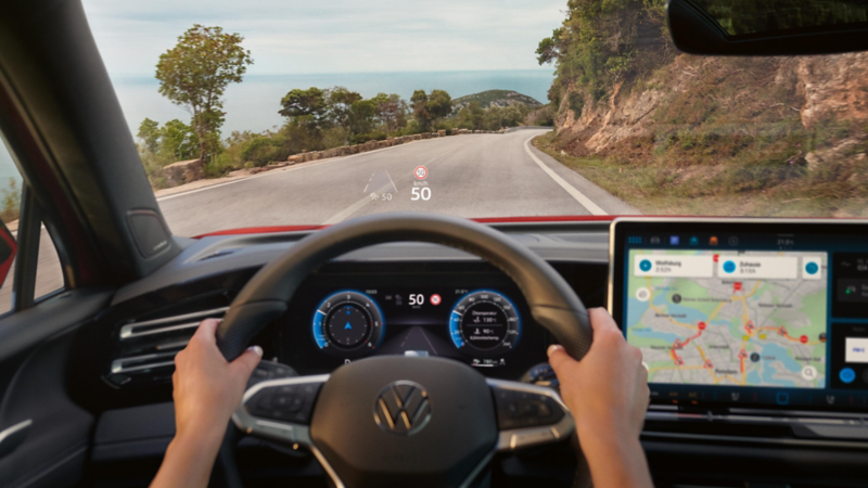 Blick auf den vorderen Innenraum des VW Golf GTI aus Sicht des Fahrers. Der Fokus liegt beim Head-Up-Display. Seitenansicht auf einen fahrenden roten Golf GTI.
