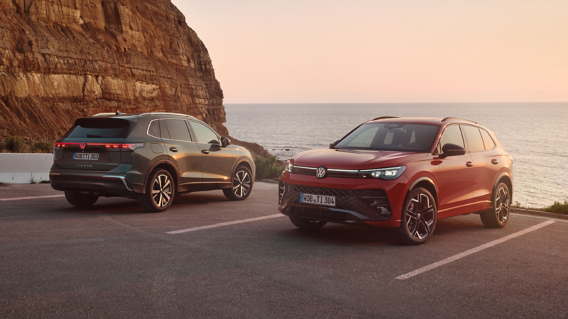 Zwei VW Tiguan in dunkelgrün und rot parken vor einer felsigen Küstenlandschaft.
