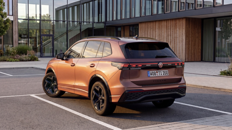 Rear view of a copper-red VW Tiguan Edition 20 parked in front of a modern building.