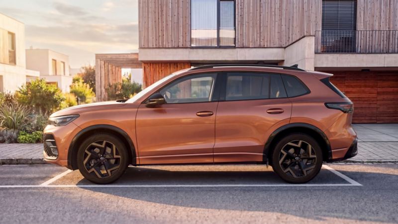 Side view of a copper-red VW Tiguan Edition 20 parked in front of a modern residential building.