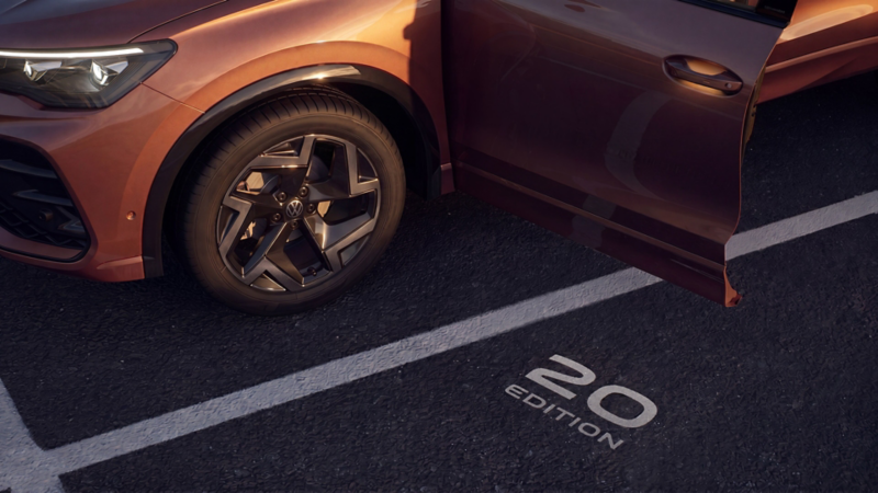 View of the open driver's door of a copper-red VW Tiguan Edition 20 with light projection of the Edition 20 lettering onto the floor.