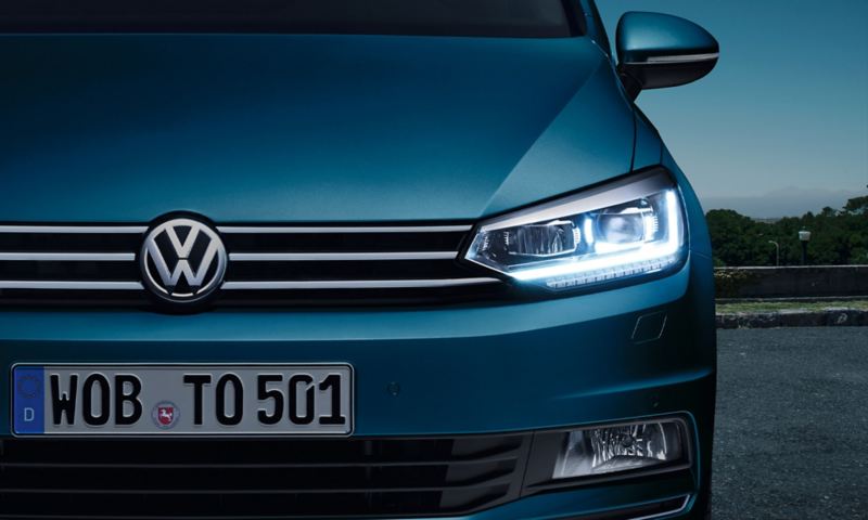 VW Touran od przodu z reflektorami ze światłami dziennymi LED, na parkingu, z tyłu obszar przemysłowy