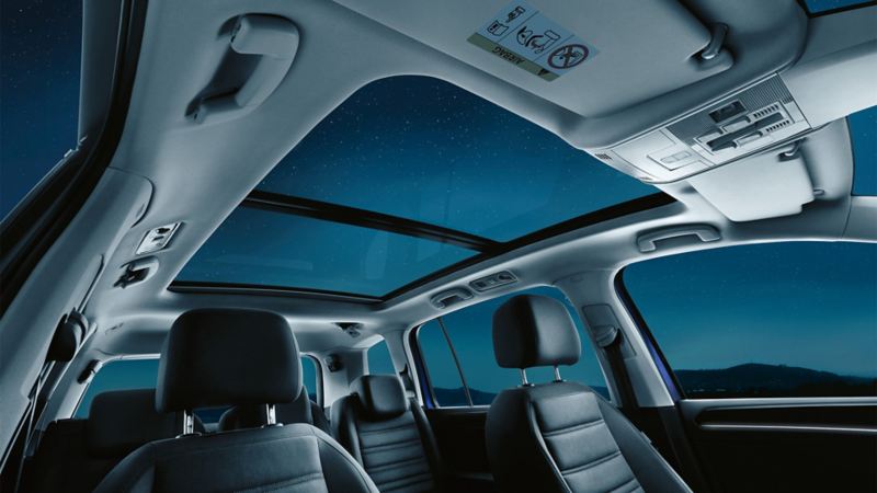 Innenraum des VW Touran mit sieben Sitzen, Fokus auf geöffnetes optionales Panoramadach, dadurch sichtbar ist der Sternenhimmel.