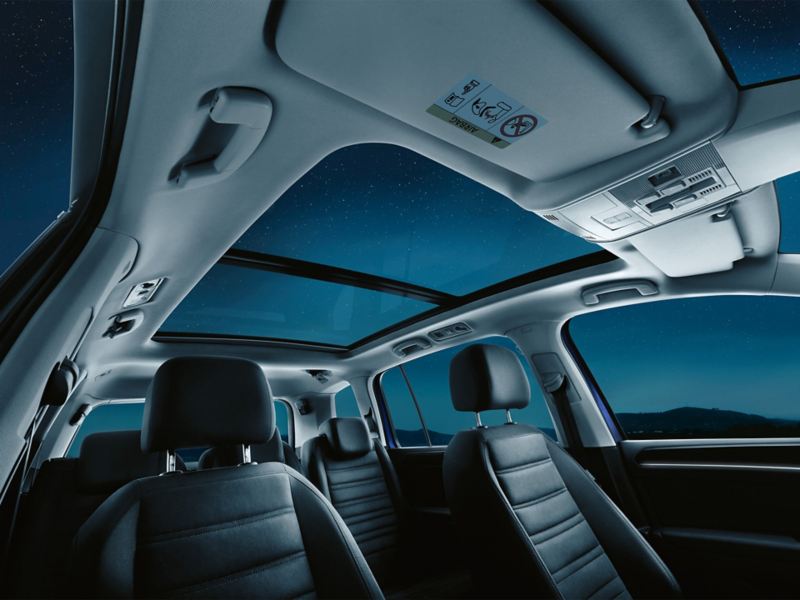Innenraum des VW Touran mit sieben Sitzen, Fokus auf geöffnetes optionales Panoramadach, dadurch sichtbar ist der Sternenhimmel.