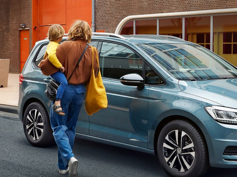 Woman carrying a child next to a blue VW