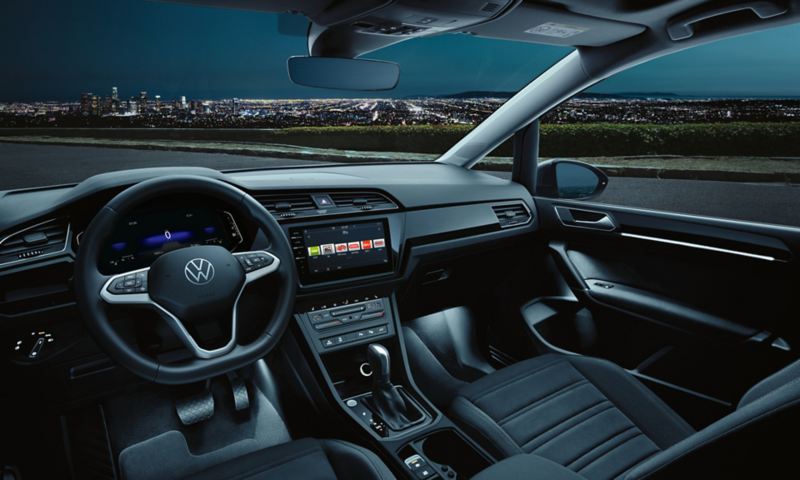 Intérieur d'un VW Touran dans l'obscurité avec l'éclairage d'ambiance optionnel activé, à l'extérieur d'une ville illuminée.