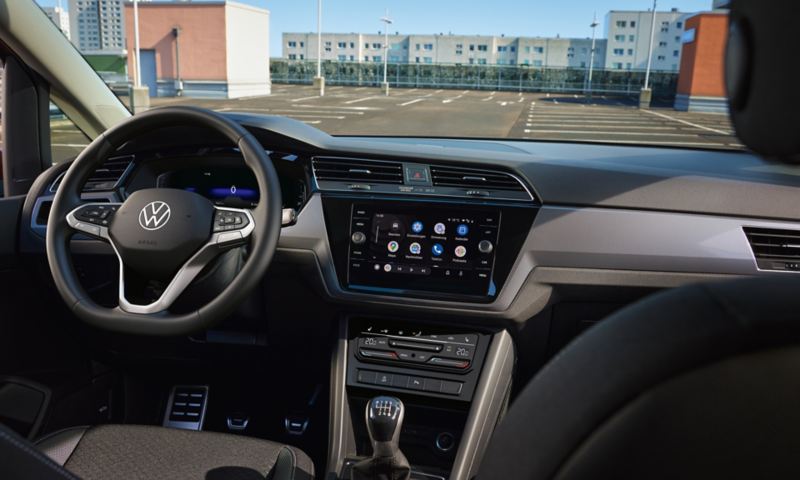 VW Touran ACTIVE innen. Blick ins Cockpit mit Multifunktionslenkrad, Farbdisplay, Sitzen und Pedalen.