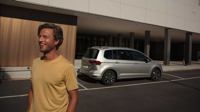 Un uomo passa davanti una Volkswagen Touran parcheggiata.