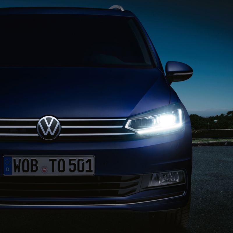 Front des VW Touran mit optionalen LED-Scheinwerfer im Fokus, markantes Design des Touran auch im Dunkeln sichtbar.