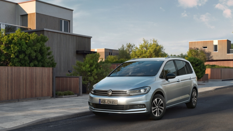 Silverner VW Touran ENERGY fährt durch Wohnstraße mit Neubauten.