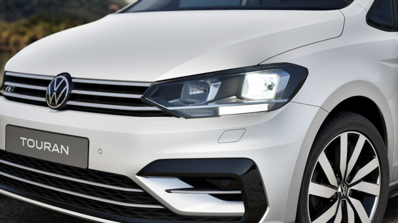 Detailaufnahme der Scheinwerfer eines weißen VW Touran ENERGY mit R-Line „Exterieur“-Paket.