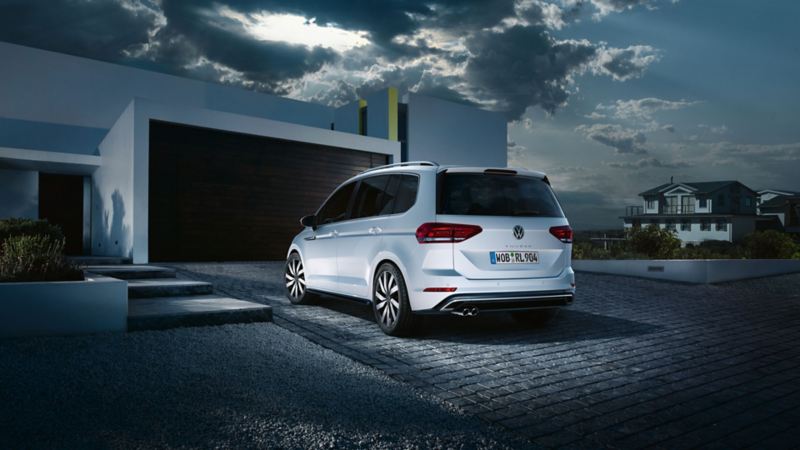 White VW Touran R-Line in the driveway of a modern house, the sporty exterior is illuminated by the sun’s rays.