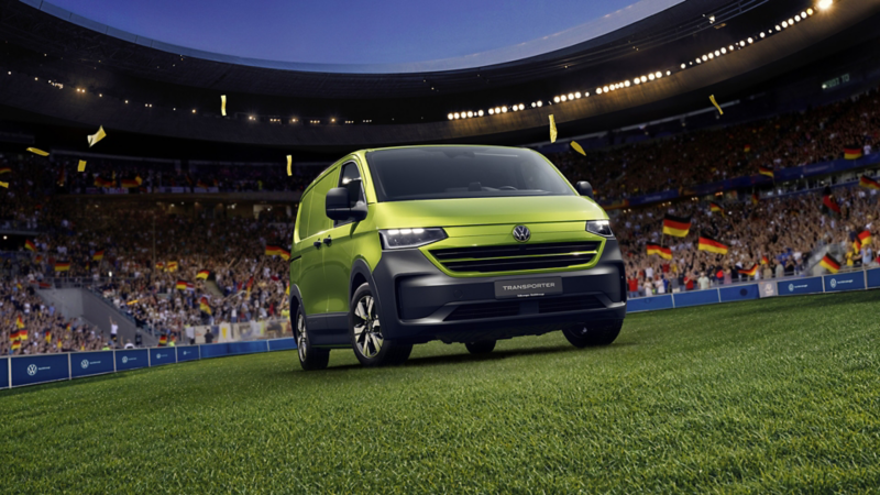 Grüner VW Transporter Kastenwagen steht auf einem Fussballfeld in einem Stadion bei Nacht.