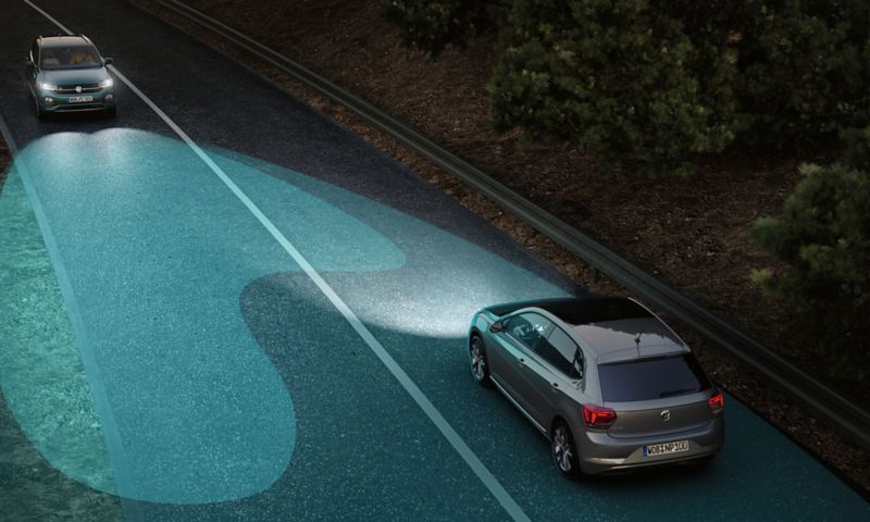 En VW T-Cross med fjernlysregulering (ekstraudstyr) kører i mørke på en vej med modkørende trafik. Lyskeglerne fra forlygterne er fremhævet.